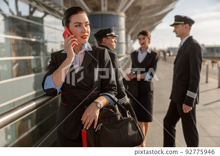 Young stewardess talking on the phone while standing with colleagues outdoors 92775946