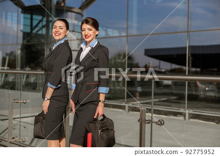 Two flight attendants with hand luggage standing outdoor 92775952