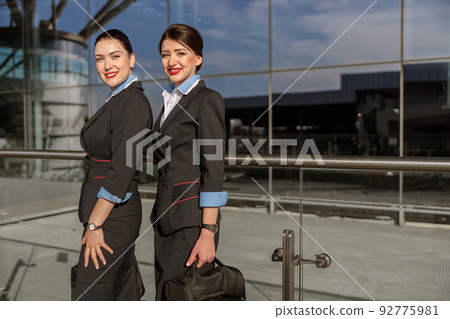Happy flight attendants with hand luggage standing near terminal 92775981