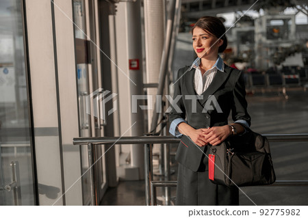 Happy beautiful female flight attendant holding bag and posing 92775982