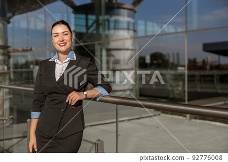 Beautiful stewardess leaning on metal rack near terminal outdoor Beautiful stewardess leaning on metal rack near terminal outdoor 92776008