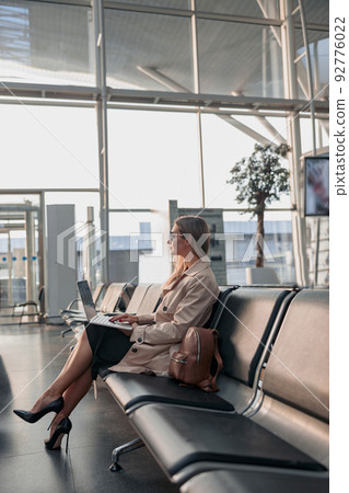 Caucasian lady typing on laptop, sitting in waiting hall at the airport Caucasian lady typing on laptop, sitting in waiting hall at the airport 92776022