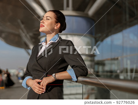 Smiling young flight attendant looking away near airport terminal Smiling young flight attendant looking away near airport terminal 92776026