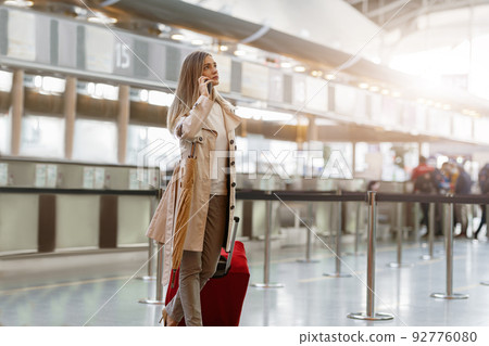 Female traveler carrying luggage bag at airport and talking phone 92776080