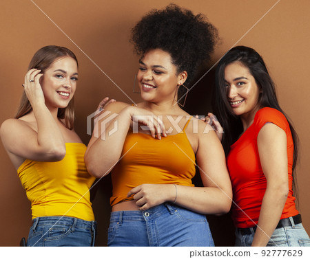 young pretty african and caucasian women posing cheerful together on brown background, lifestyle diverse nationality people concept close up 92777629