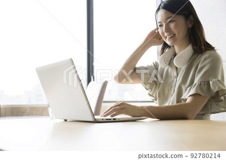 A young woman working on a computer with a neck fan at a restaurant 92780214