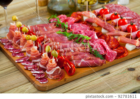 Slicing sausages and ham with cherry tomatoes and olives on board 92781611