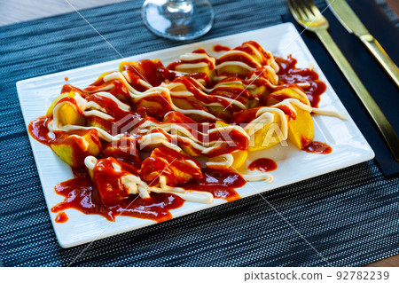 Prepared patatas bravas with sauce served on plate on wooden table 92782239