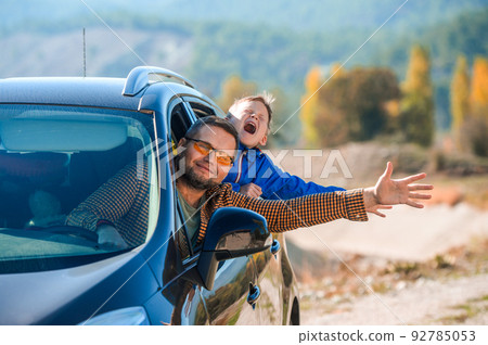 Happy family travel by car in the mountains. Summer vacation concept. Happy boy and father looking out from auto window and greets nature 92785053
