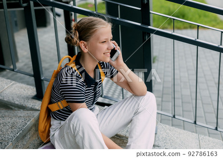 A beautiful girl is sitting on the stairs at school in between classes and talking on the phone 92786163