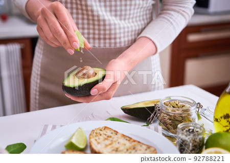 Woman squeezing fresh lime juice on a halved avocado at domestic kitchen 92788221