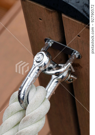 Stainless shackles and white ropes attached to a wooden railing in a sea marina with rain drops Stainless shackles and white ropes attached to a wooden railing in a sea marina with rain drops 92790572