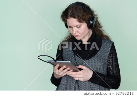 A woman with curly hair carefully looks at a digital tablet that she holds in her hands A woman with curly hair carefully looks at a digital tablet that she holds in her hands 92792218