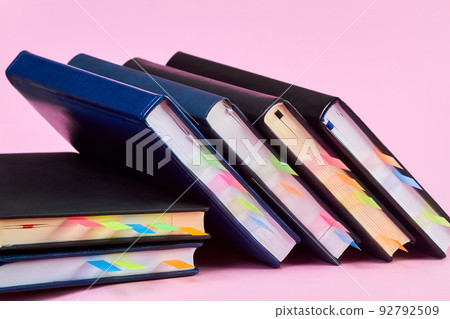 Close-up of a stack of office notepads with colorful sticky page markers sandwiched between pages on pink background Close-up of a stack of office notepads with colorful sticky page markers sandwiched between pages on pink background 92792509