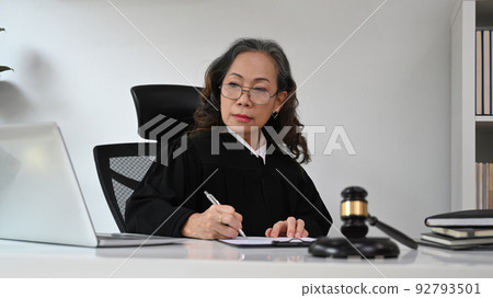 Focused mature female judge sitting front of laptop, talking to her clients for providing law consultation and legal advice online Focused mature female judge sitting front of laptop, talking to her clients for providing law consultation and legal advice online 92793501