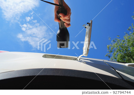hand of woman plugging in an electric car at outlet socket. 92794744