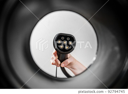 hand of woman plugging in an electric car at outlet socket. 92794745