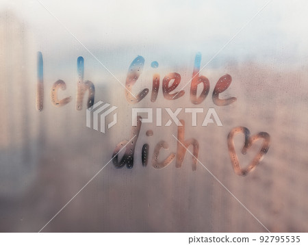 Lettering Deutsch text Ich liebe dich I love you in english and heart shape on sunset wet window 92795535