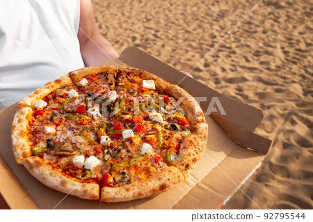 Pizza with mushrooms, tomatoes and mozzarella lies in brown paper box in male hands Pizza with mushrooms, tomatoes and mozzarella lies in brown paper box in male hands 92795544