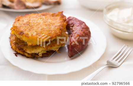 Fried grated potato pancakes with fried sausage on white plate 92796566