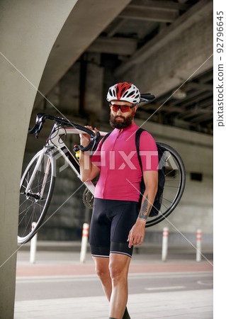 Portrait of a cyclist standing under a bridge with a bicycle in his hand, posing at the camera against an architecture background. Active lifestyle. Cycling is a hobby. Portrait of a cyclist standing under a bridge with a bicycle in his hand, posing at the camera against an architecture background. Active lifestyle. Cycling is a hobby. 92796645