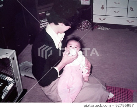 1970 年代的日本：一位母親在房間裡餵她 0 歲的女兒 92796997