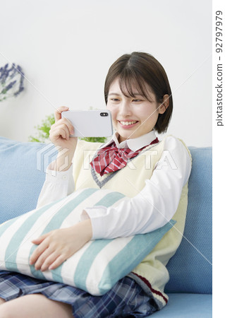 A high school girl watching a video on her smartphone at home A high school girl watching a video on her smartphone at home 92797979
