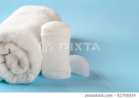 Solid antiperspirant deodorant and rolled bath towel on a blue background.  92798034