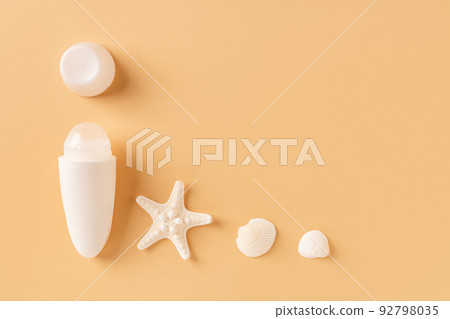 Open roll on antiperspirant deodorant, sea star and shells against pastel orange background. 92798035