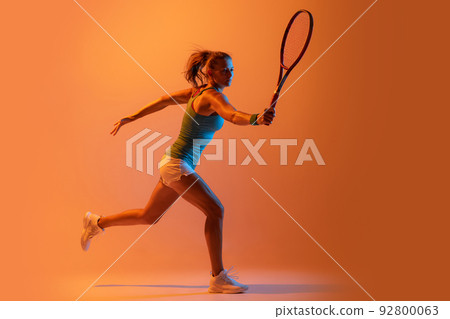 Portrait of sportive woman, professional tennis player training isolated over orange studio background in neon light Portrait of sportive woman, professional tennis player training isolated over orange studio background in neon light 92800063