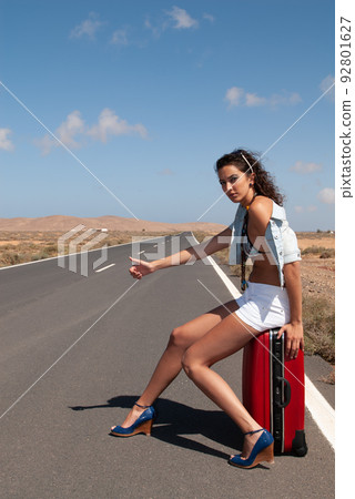 attractive woman hitchhiking on a lonely road attractive woman hitchhiking on a lonely road 92801627