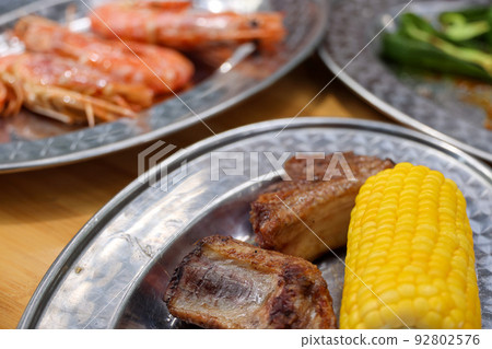 Camping BBQ charcoal-grilled feast: shrimp, corn, green peppers, and grilled meat 92802576