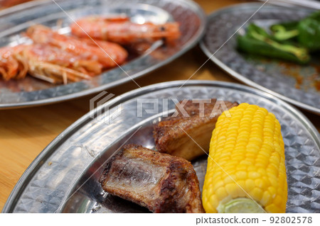 Camping BBQ charcoal-grilled feast: shrimp, corn, green peppers, and grilled meat 92802578