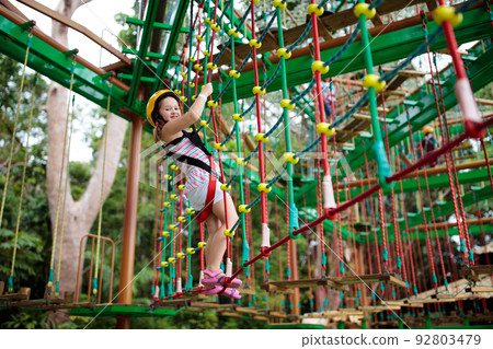 Child in adventure park. Kids climbing rope trail. 92803479