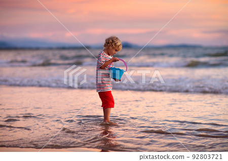 Child playing on ocean beach. Kid at sunset sea. 92803721