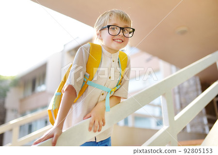 Smart little child with backpack on the stairs of school building. Quality education for children. Portrait of funny nerd schoolboy with big glasses. Vision problems. Back to school concept. Smart little child with backpack on the stairs of school building. Quality education for children. Portrait of funny nerd schoolboy with big glasses. Vision problems. Back to school concept. 92805153