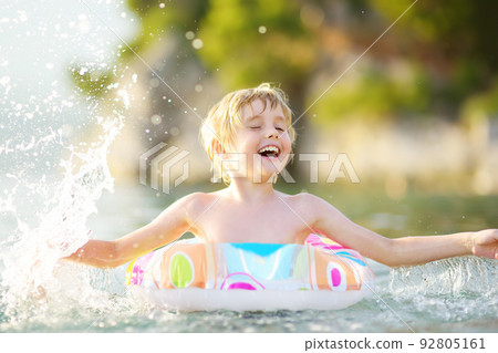 Little boy swimming with colorful floating ring in sea on sunny summer day. Cute child playing on beach. Family and children's resort holiday during summer vacations. 92805161