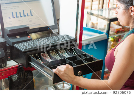 latina woman looking disappointed at the cash register of her business to see how much money there is. girl working in latin american neighborhood store. economy and business concept. 92806076