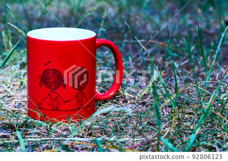 Red ceramic cup inscription love and funny couple on green grass in the park Red ceramic cup inscription love and funny couple on green grass in the park 92806123