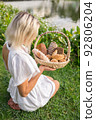 Young woman in white dress sitting on the grass with basket with assorti of brown and white homemade bread. High quality photo 92806204
