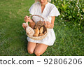 Young woman in white dress sitting on the grass with basket with assorti of brown and white homemade bread. High quality photo 92806206
