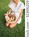 Young woman in white dress sitting on the grass with basket with assorti of brown and white homemade bread. High quality photo 92806209