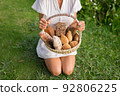 Young woman in white dress sitting on the grass with basket with assorti of brown and white homemade bread. High quality photo 92806225