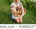 Young woman in white dress sitting on the grass with basket with assorti of brown and white homemade bread. High quality photo 92806227