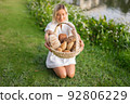 Young woman in white dress sitting on the grass with basket with assorti of brown and white homemade bread. High quality photo 92806229