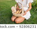 Young woman in white dress sitting on the grass with basket with assorti of brown and white homemade bread. High quality photo 92806231