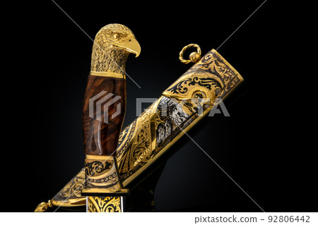 souvenir collectible silver gold dagger cutlass with scabbard, with metal engraving, on black background. Luxury weapons with traditional patterns in medieval vintage style. souvenir collectible silver gold dagger cutlass with scabbard, with metal engraving, on black background. Luxury weapons with traditional patterns in medieval vintage style. 92806442
