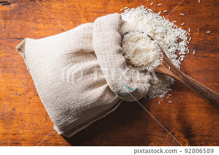Uncooked white rice in burlap sack on wooden table. Uncooked white rice in burlap sack on wooden table. 92806589