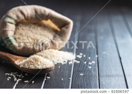 Uncooked white rice on wooden spoon on black table. Uncooked white rice on wooden spoon on black table. 92806597
