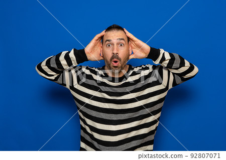 Stunned latin man with his head in his hands with a surprised expression isolated on blue background. Stunned latin man with his head in his hands with a surprised expression isolated on blue background. 92807071